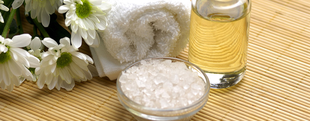 Bamboo mat with massage oil, scented salt crystals, fresh cut flowers, and a white towel.